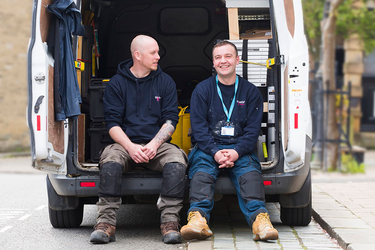 Two men in work boots sitting in the back of a van