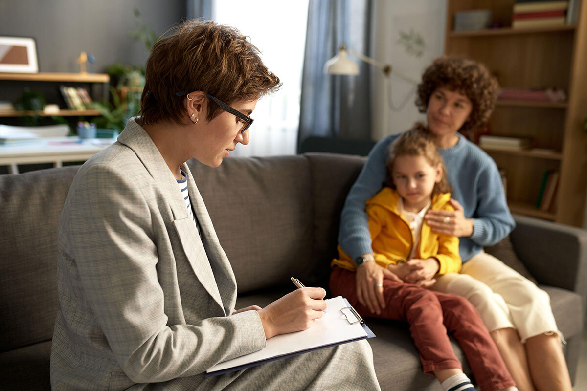 A social worker making notes while talking to a child and their mum at home 