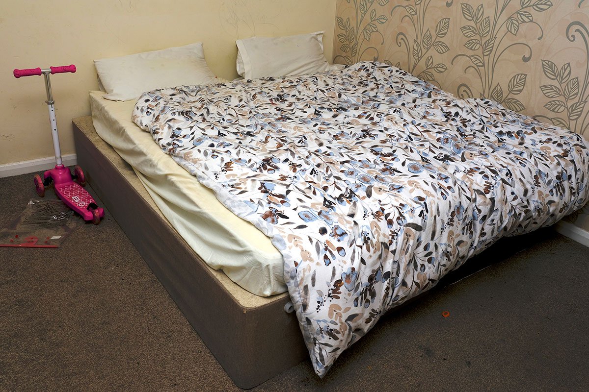 A bed in temporary accommodation with a child’s scooter