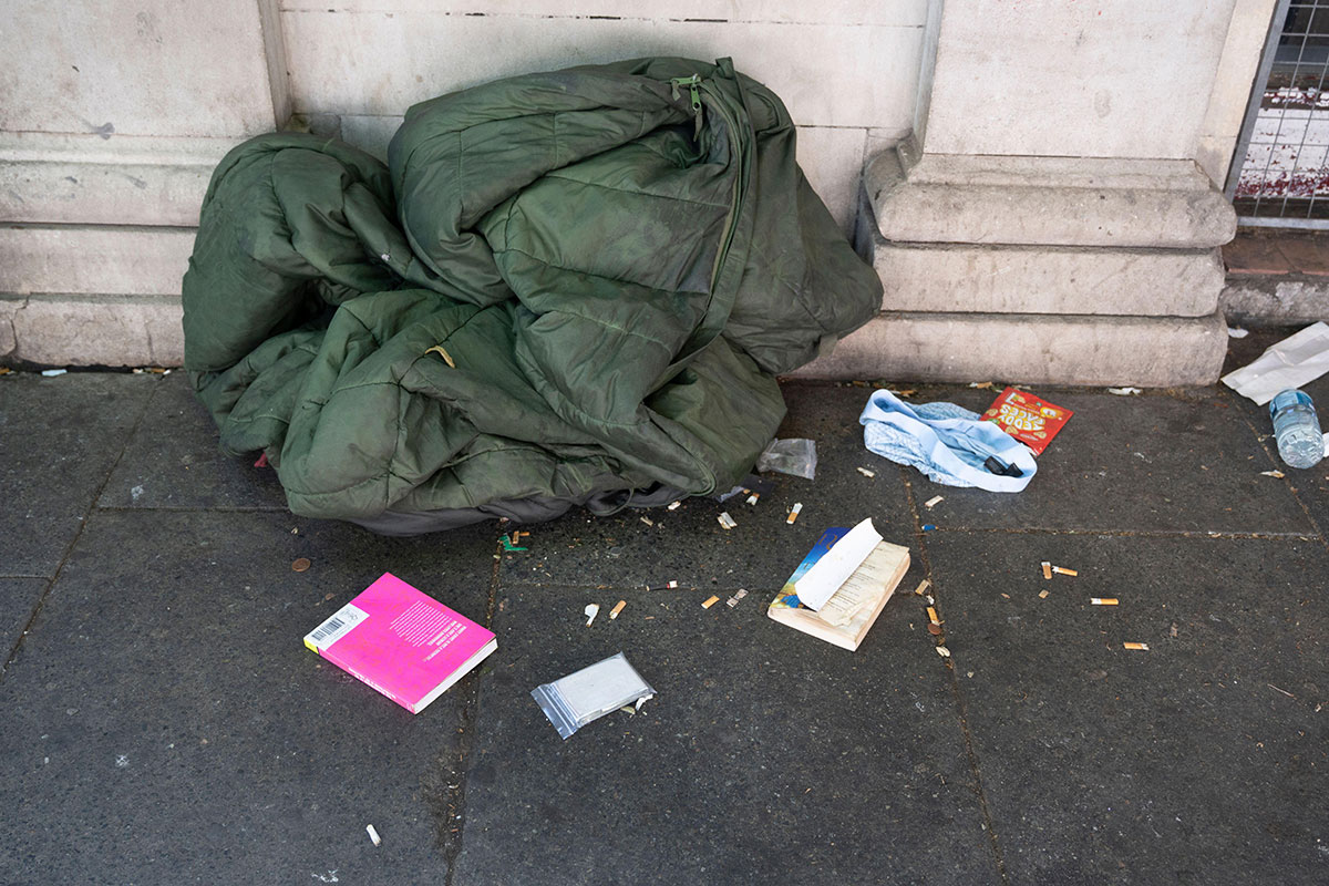 Sleeping bag on pavement, surrounded by cigarette butts