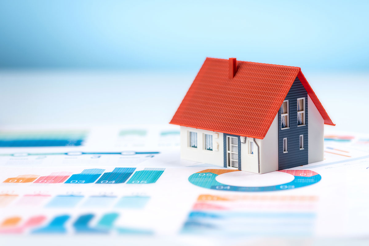 Small plastic model of a house on top of a piece of paper with graphs and pie charts on it