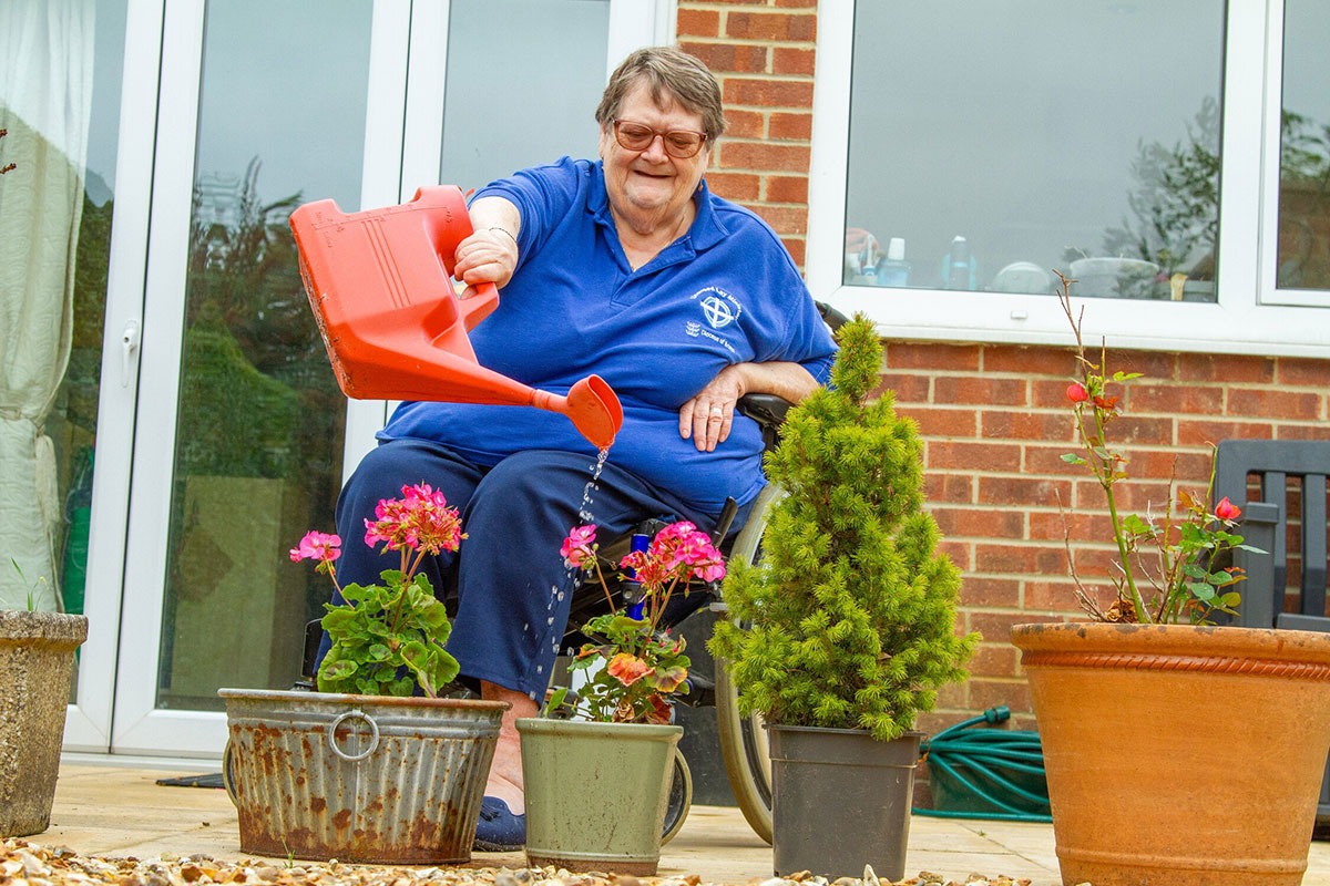 An older person in a wheelchair watering plants An older person in a wheelchair watering plants