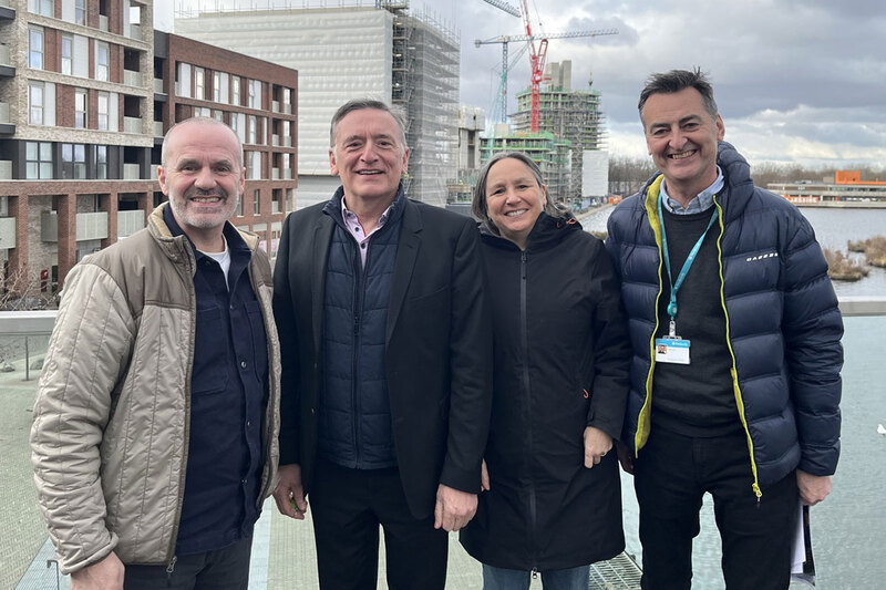 Four people posing for a picture next to several buildings under construction