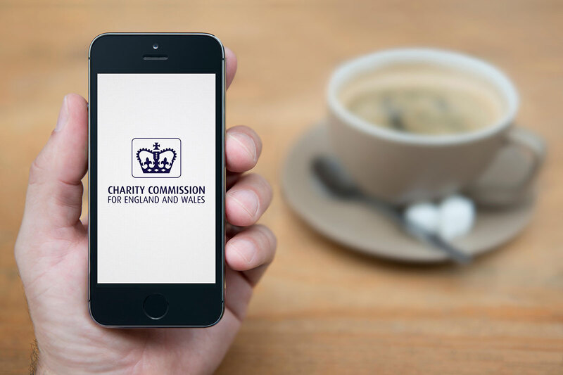 A phone screen showing the Charity Commission homepage, next to a hot drink