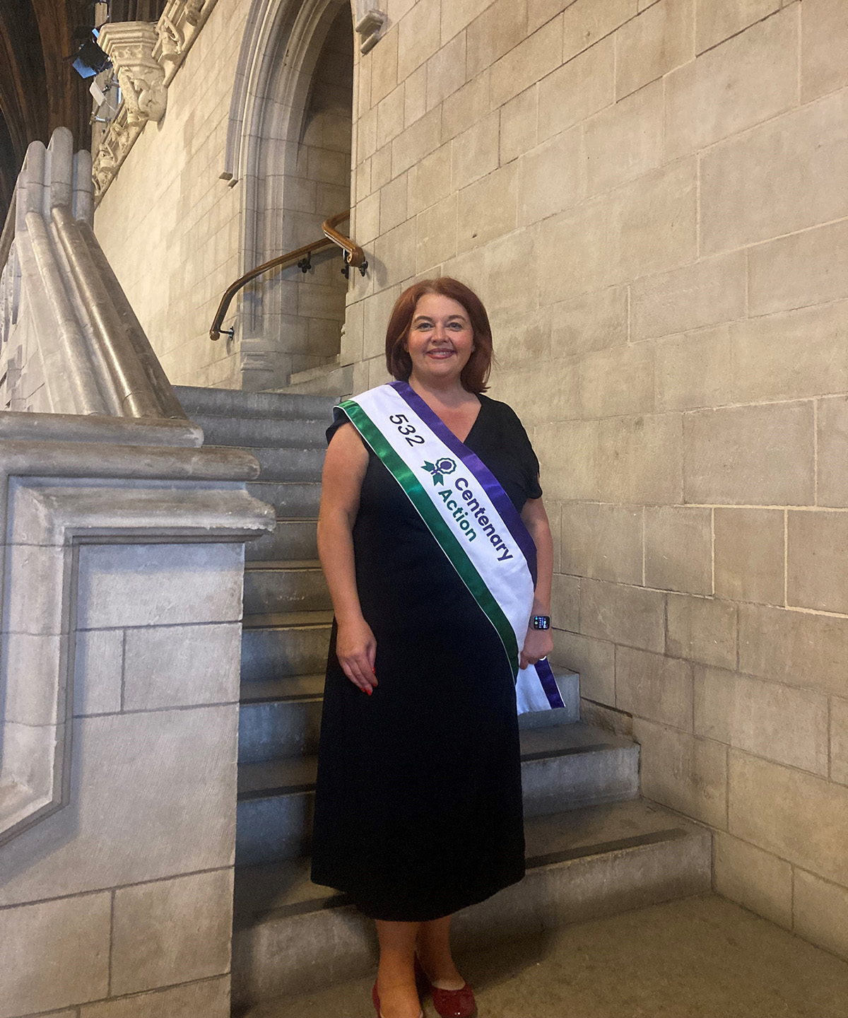 Paula Barker wearing a sash in Suffragette colours reading “Centenary Action” Paula Barker wearing a sash in Suffragette colours reading “Centenary Action”