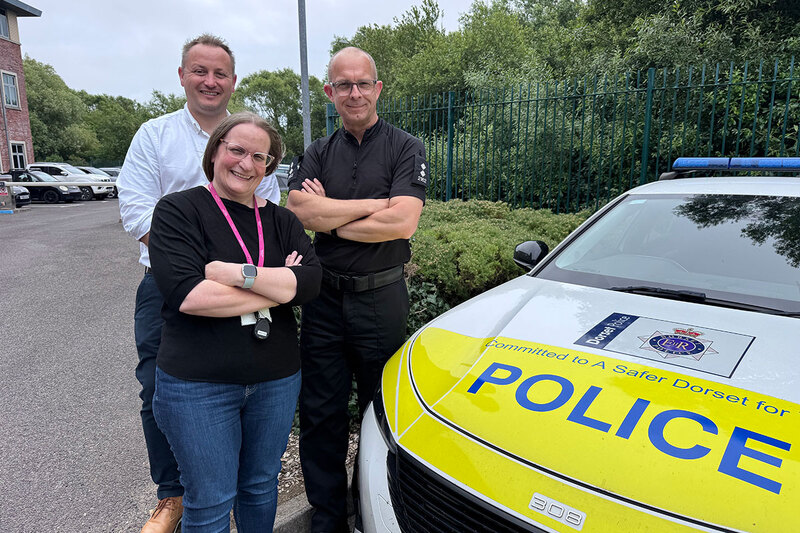 Three people posing next to a police car